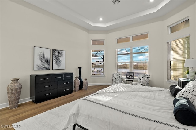 bedroom with recessed lighting, wood finished floors, baseboards, visible vents, and a tray ceiling