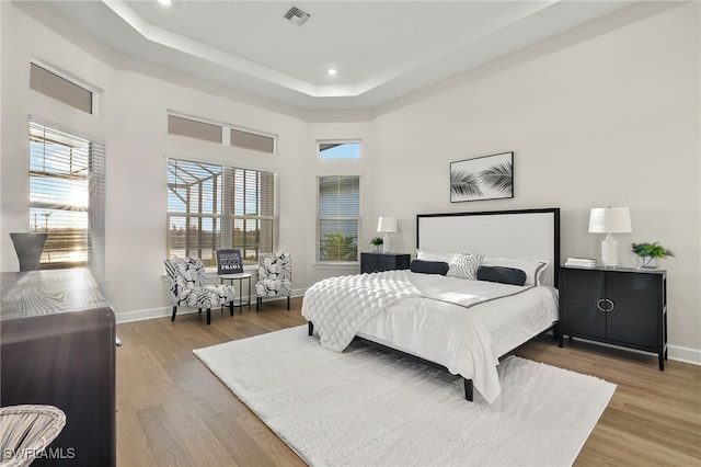 bedroom with visible vents, a tray ceiling, light wood-style flooring, and baseboards