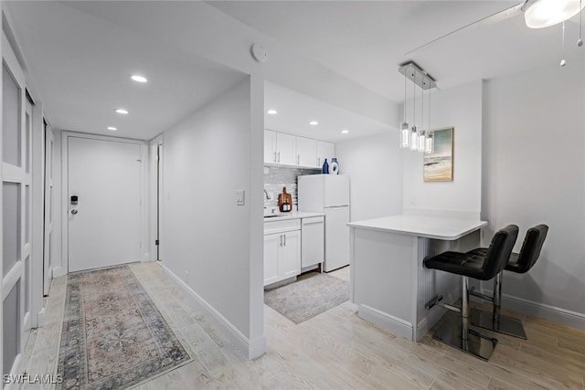 kitchen featuring white appliances, tasteful backsplash, kitchen peninsula, white cabinetry, and light hardwood / wood-style floors