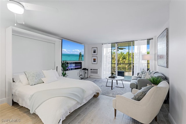 bedroom featuring hardwood / wood-style flooring, access to outside, a wall mounted air conditioner, and a wall of windows