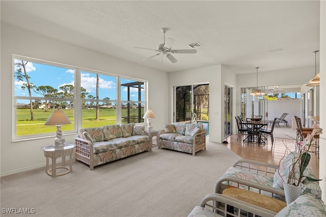 carpeted living room with a healthy amount of sunlight, baseboards, ceiling fan with notable chandelier, and visible vents