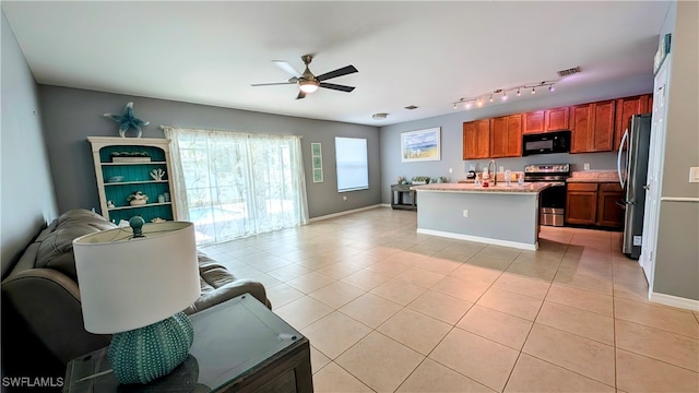 kitchen with stainless steel appliances, ceiling fan, sink, light tile patterned floors, and a center island with sink