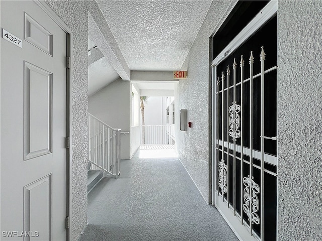 corridor featuring lofted ceiling, a textured ceiling, and carpet flooring