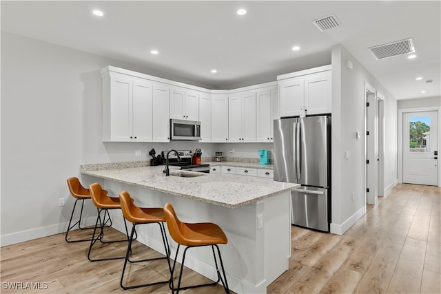 kitchen with appliances with stainless steel finishes, a breakfast bar, white cabinetry, light hardwood / wood-style flooring, and sink