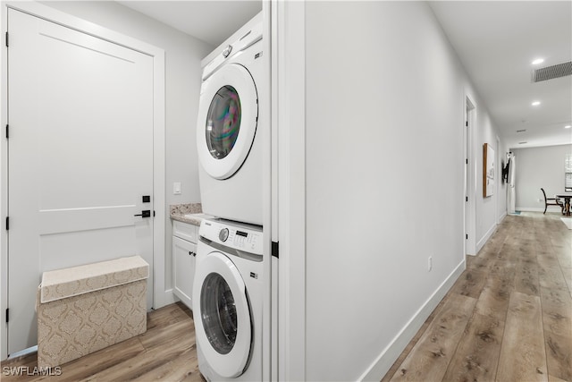 laundry room with stacked washer and clothes dryer, light hardwood / wood-style floors, and cabinets