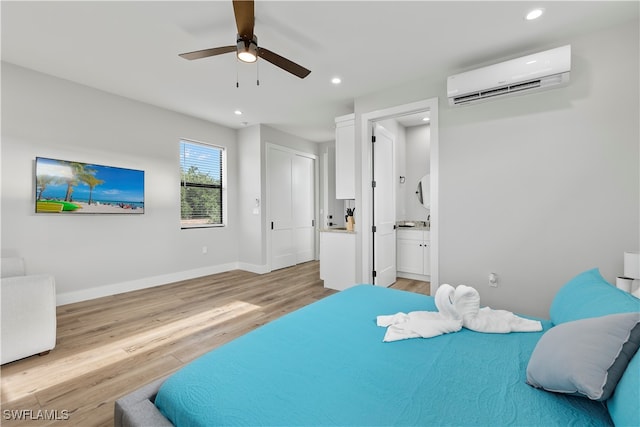 bedroom with ensuite bathroom, a wall mounted air conditioner, light wood-type flooring, and ceiling fan