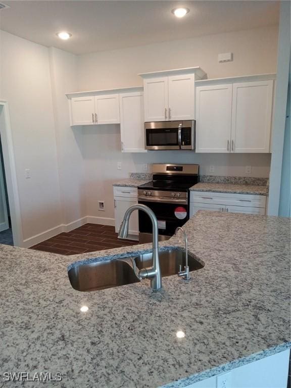 kitchen with stainless steel appliances, light stone countertops, white cabinets, and sink