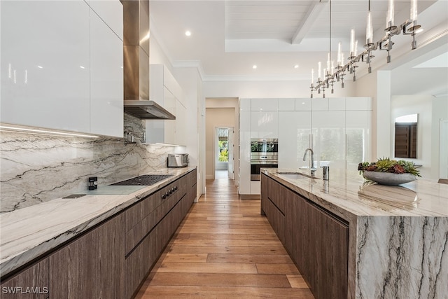 kitchen featuring white cabinets, hanging light fixtures, light hardwood / wood-style floors, wall chimney exhaust hood, and sink