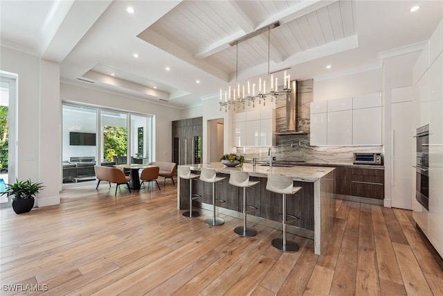 kitchen with light hardwood / wood-style flooring, a center island with sink, white cabinets, and a tray ceiling