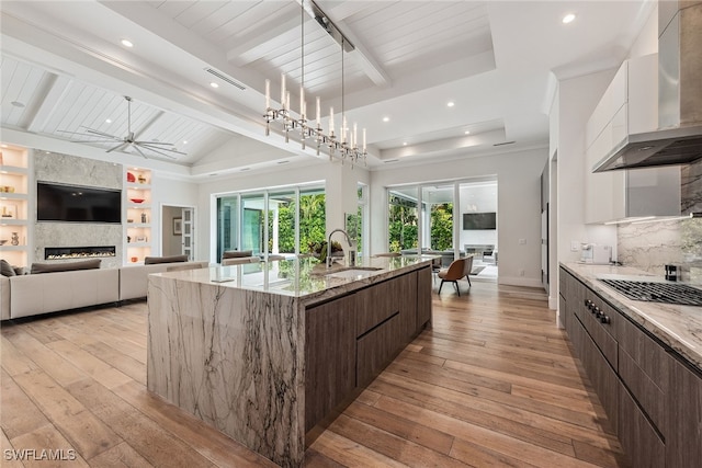 kitchen featuring wall chimney range hood, a spacious island, sink, light hardwood / wood-style floors, and decorative light fixtures