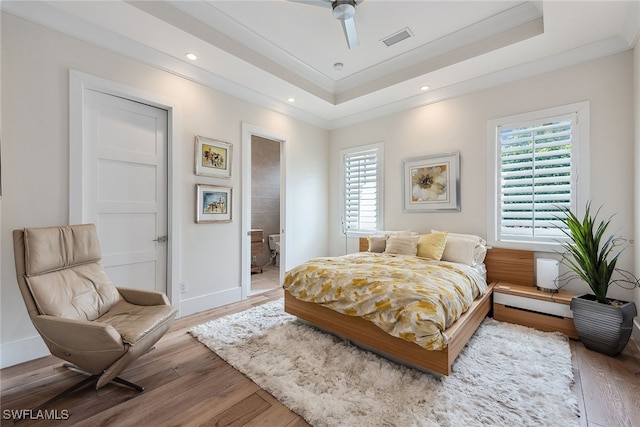 bedroom featuring ensuite bath, a tray ceiling, ceiling fan, hardwood / wood-style flooring, and ornamental molding