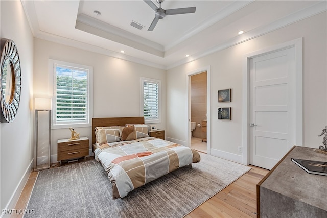 bedroom with ensuite bath, a raised ceiling, ceiling fan, crown molding, and light hardwood / wood-style flooring