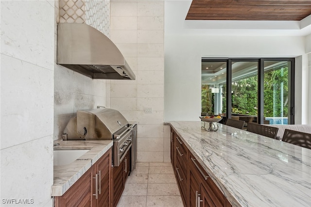 kitchen featuring wall chimney exhaust hood, tile walls, sink, and light stone countertops