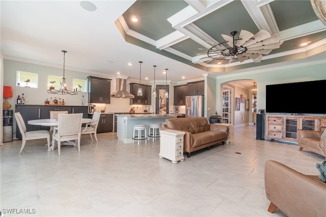 tiled living room with crown molding, a tray ceiling, and a chandelier