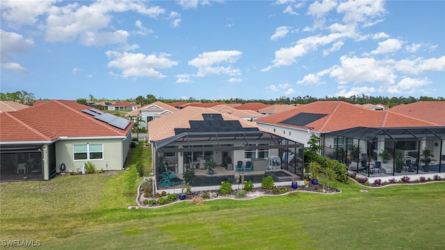 back of house with solar panels, a lanai, and a lawn