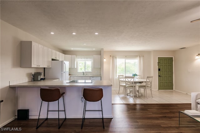 kitchen featuring white appliances, wood-type flooring, kitchen peninsula, white cabinetry, and a breakfast bar