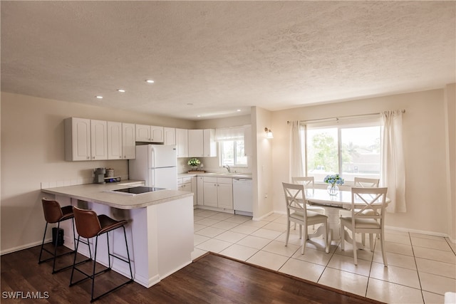 kitchen featuring white appliances, sink, kitchen peninsula, white cabinetry, and light hardwood / wood-style flooring