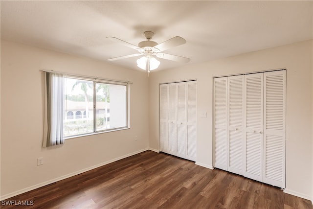 unfurnished bedroom with dark hardwood / wood-style flooring, multiple closets, and ceiling fan