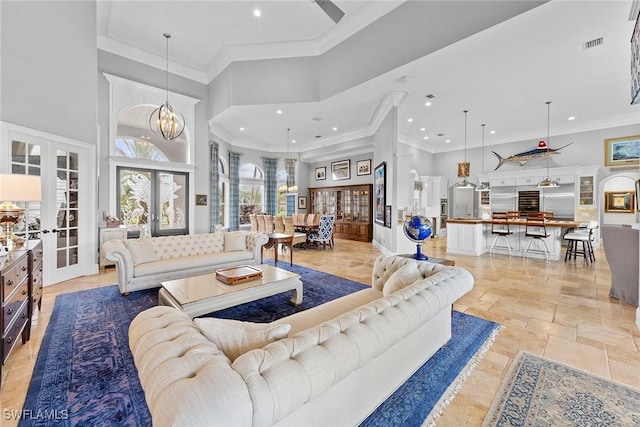 living room with a notable chandelier, crown molding, french doors, and a high ceiling