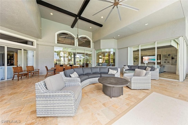 living room with a towering ceiling, beamed ceiling, and ceiling fan