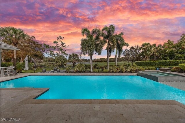 pool at dusk with an in ground hot tub and a patio