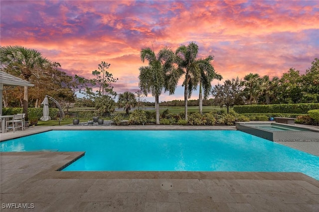 pool at dusk featuring an in ground hot tub and a patio area