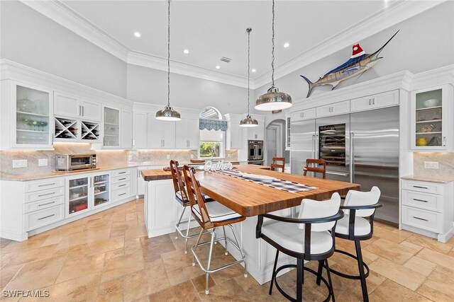 kitchen featuring decorative backsplash, stainless steel appliances, white cabinets, a high ceiling, and hanging light fixtures