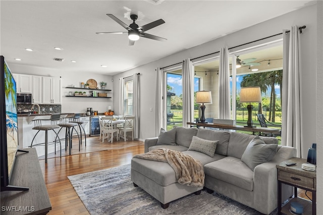 living room with ceiling fan, light wood-type flooring, sink, and beverage cooler