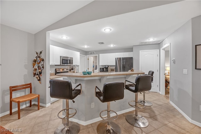 kitchen with a breakfast bar, lofted ceiling, light tile patterned floors, appliances with stainless steel finishes, and white cabinetry