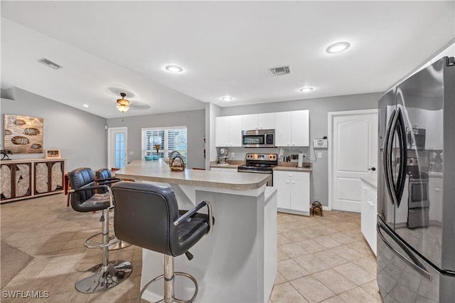 kitchen featuring a center island with sink, a breakfast bar area, ceiling fan, white cabinetry, and stainless steel appliances