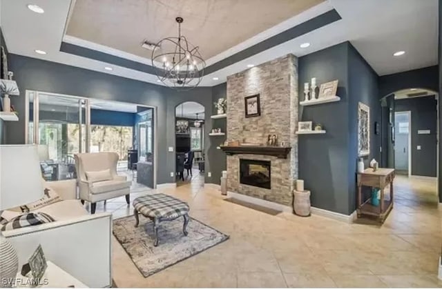 living room with a stone fireplace, an inviting chandelier, and a raised ceiling