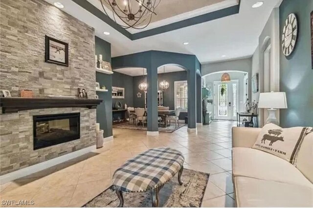 tiled living room featuring a chandelier, a tray ceiling, and a fireplace