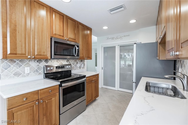 kitchen with tasteful backsplash, appliances with stainless steel finishes, sink, and light stone counters