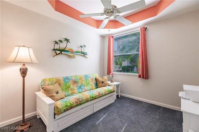 living area with ceiling fan, a tray ceiling, and dark carpet