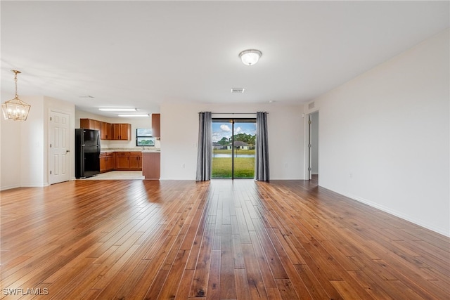 unfurnished living room featuring a notable chandelier and light hardwood / wood-style floors