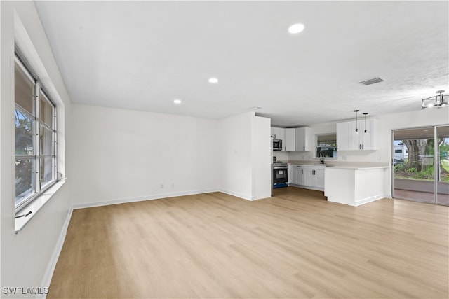 unfurnished living room featuring sink, light wood-type flooring, and a wealth of natural light