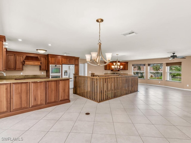 kitchen featuring hanging light fixtures, white refrigerator with ice dispenser, premium range hood, light tile patterned floors, and ceiling fan with notable chandelier