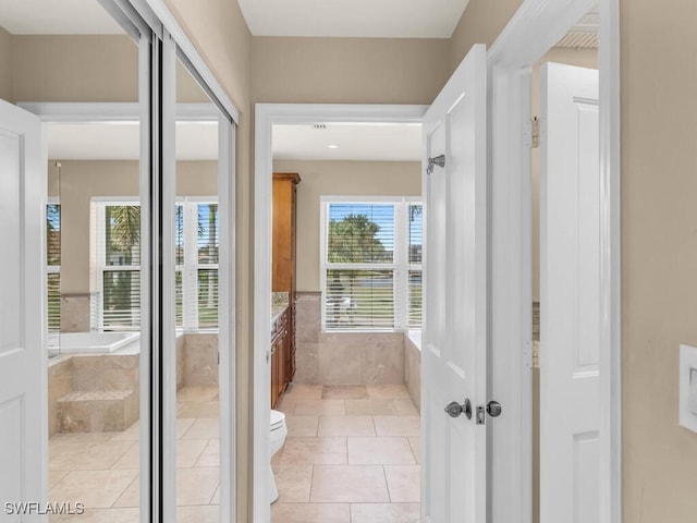 bathroom featuring tile patterned floors, tiled tub, toilet, and a wealth of natural light