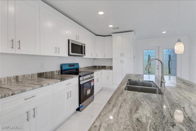 kitchen featuring stainless steel appliances, light stone counters, white cabinets, sink, and pendant lighting