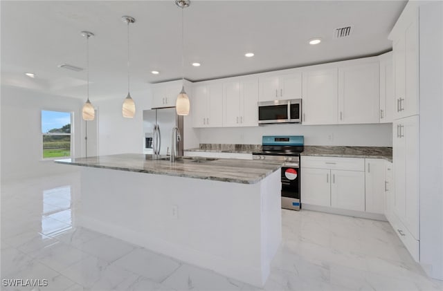 kitchen featuring a center island with sink, white cabinetry, appliances with stainless steel finishes, hanging light fixtures, and dark stone countertops