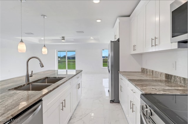 kitchen featuring white cabinetry, appliances with stainless steel finishes, decorative light fixtures, light stone countertops, and sink