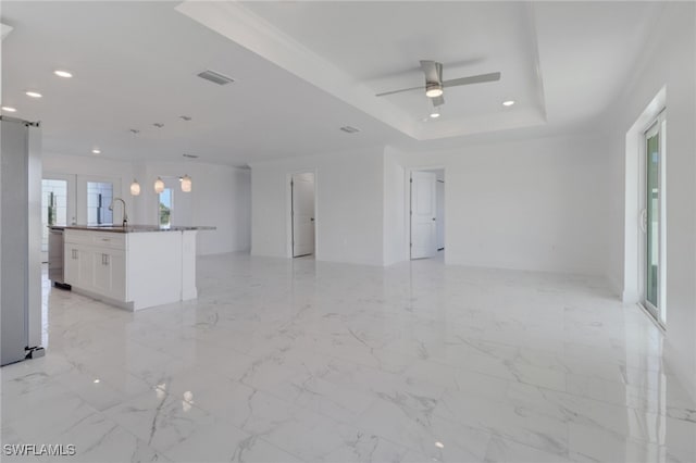 unfurnished living room with ceiling fan, sink, and a raised ceiling