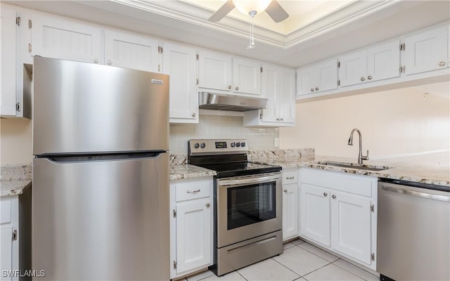 kitchen with a tray ceiling, stainless steel appliances, white cabinetry, a sink, and under cabinet range hood