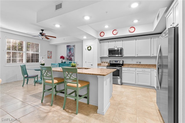 kitchen featuring a kitchen bar, a center island, white cabinetry, stainless steel appliances, and light stone counters