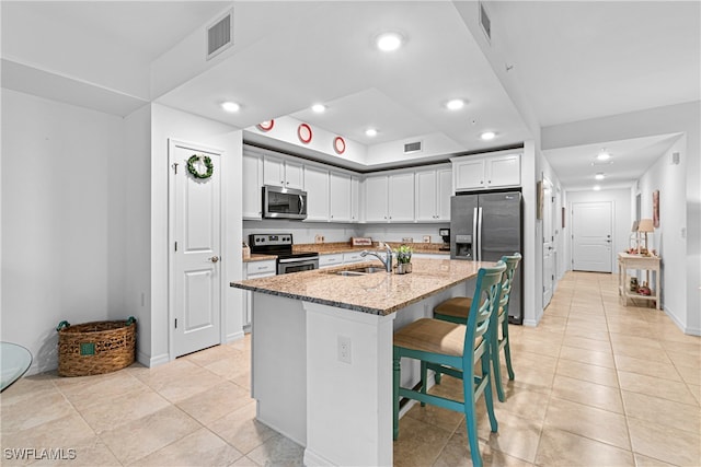 kitchen with a center island with sink, light stone counters, appliances with stainless steel finishes, a kitchen breakfast bar, and sink