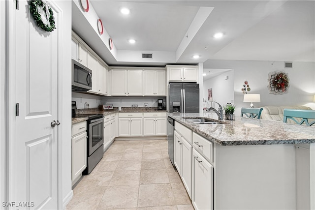 kitchen with light stone countertops, appliances with stainless steel finishes, sink, white cabinets, and a kitchen island with sink