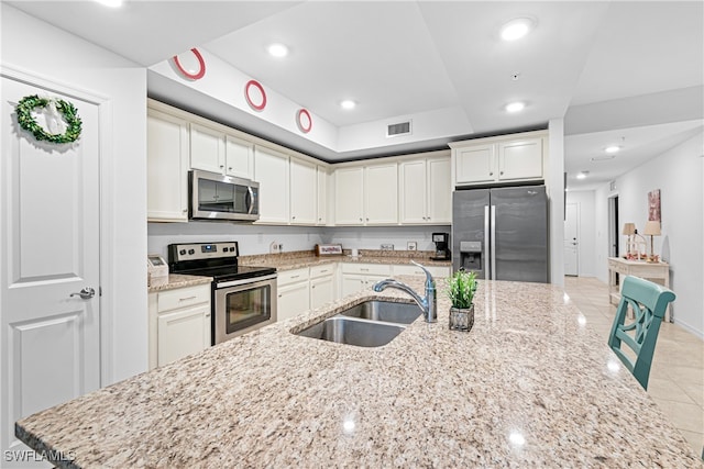 kitchen featuring appliances with stainless steel finishes, white cabinetry, light stone countertops, and sink