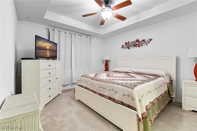 bedroom with light colored carpet, a raised ceiling, and ceiling fan