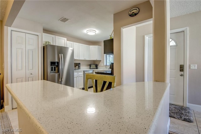 kitchen featuring light tile patterned flooring, appliances with stainless steel finishes, white cabinets, and light stone counters