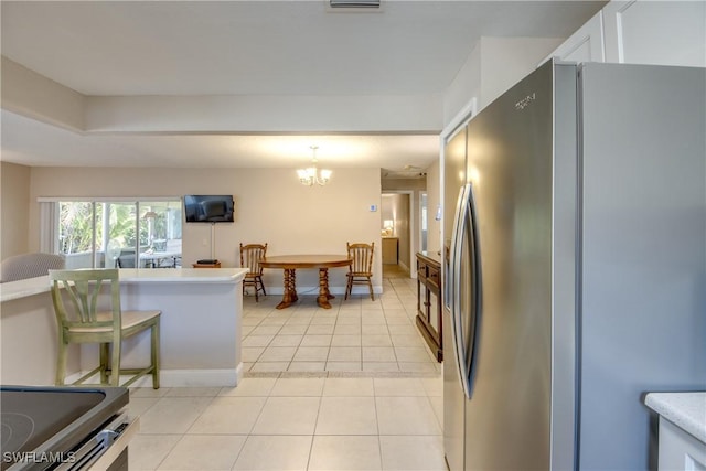 kitchen featuring light tile patterned flooring, a breakfast bar, white cabinetry, stainless steel fridge, and an inviting chandelier